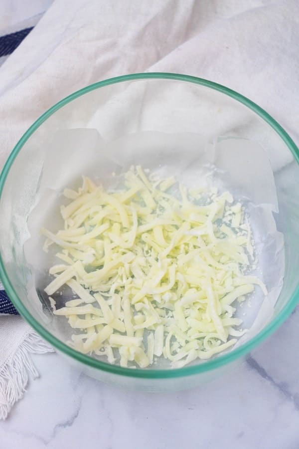 shredded mozzarella in a glass bowl on a white cloth
