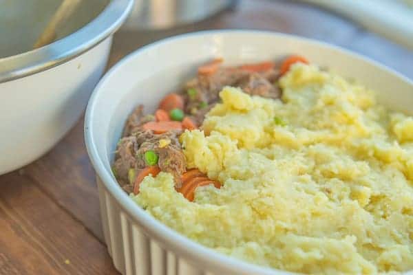 shepherd's pie in a white casserole dish next to a bowl on a wood table