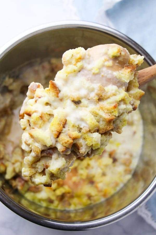 a wooden spoon holding chicken and stuffing above an instant pot with more of the same food in it