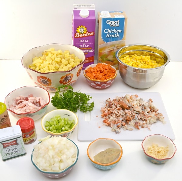 containers of half and half, chicken broth, pepper and other spices, bowls of diced potatoes, carrots, corn, salt pork, celery, onions, garlic, a bay leaf, and lobster meat on a cutting board