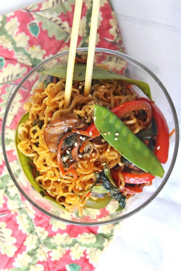 overhead view of teriyaki veggie stir fry and chopsticks in a glass bowl on a red flowered cloth 