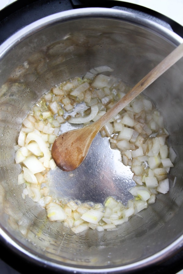 butter, chopped onions, and garlic cooking in an instant pot with a wooden spoon