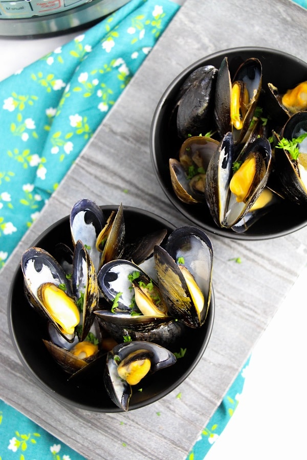 mussels in black bowls on a wood board with an instant pot in the background 