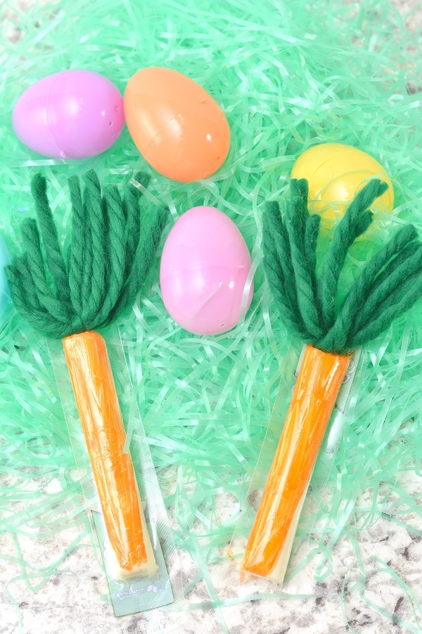 cheese sticks colored orange with green yarn at the top to look like carrots on fake grass next to plastic eggs 