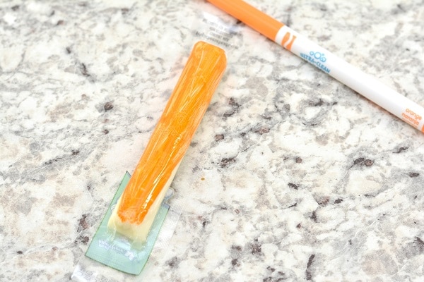 a cheese stick colored orange next to an orange marker on a gray counter