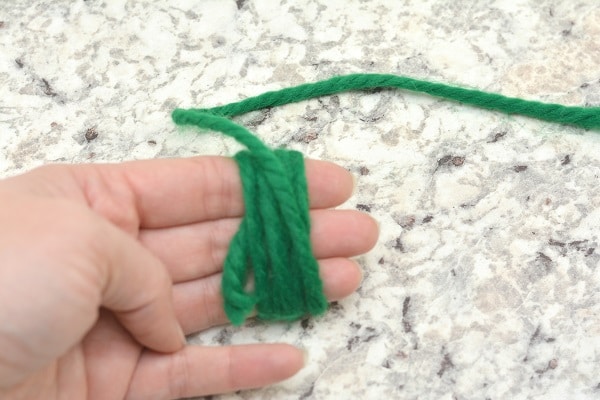 a hand with green yarn wrapped around the fingers on a gray counter