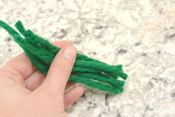 a hand holding green pieces of yarn on a gray counter