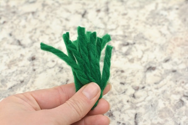 a hand holding green pieces of yarn on a gray counter