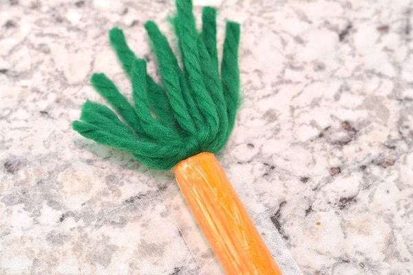 a cheese stick colored orange with green yarn at the top to look like a carrot on a gray counter