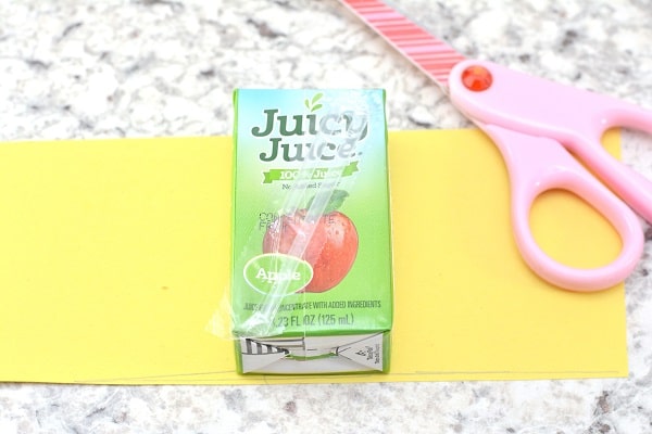 a juicy juice box on a yellow construction paper next to pink scissors on a gray kitchen counter