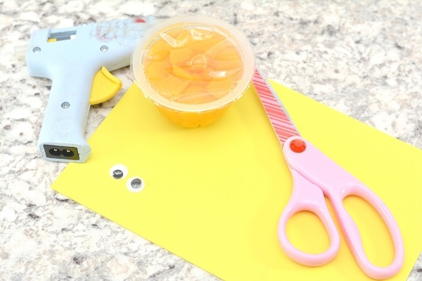 snack cup (I used peaches), yellow craft foam, googly eyes, scissors, and a low-temperature glue gun on a gray counter