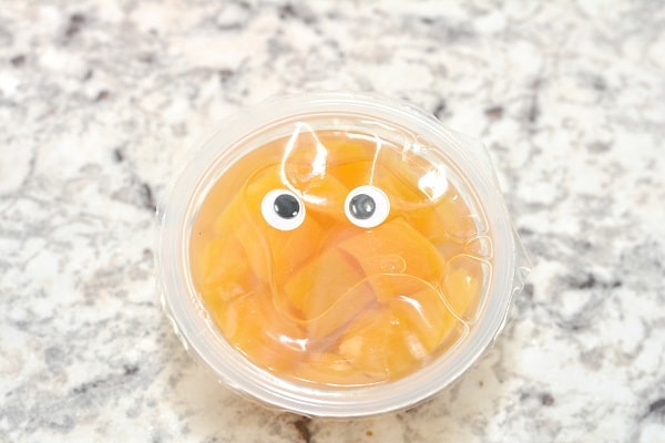 a peach fruit cup with googly eyes on it on a gray counter