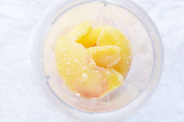 overhead view of frozen peach slices in a cup on a white background