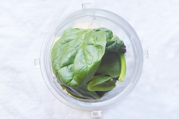 overhead view of frozen peach slices and spinach leaves in a cup on a white background