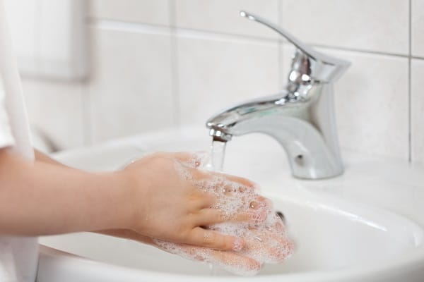 a child washing their hands at a sink in a white bathroom