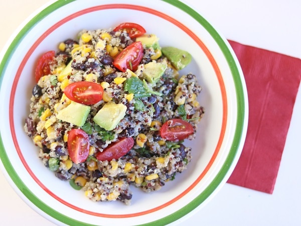 quinoa black bean salad in a white, orange and green bowl on a red napkin on a white table
