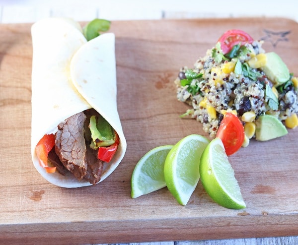 sous vide beef fajitas on a wood cutting board next to slices of lime and a quinoa side dish