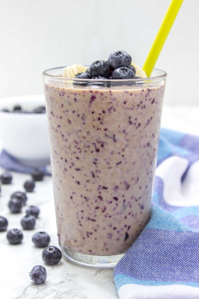 blueberry banana chia smoothie in a glass with a yellow straw in it with more blueberries on the table next to it