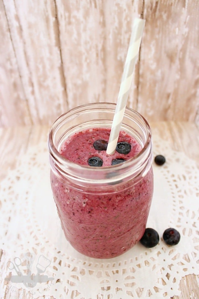 a blueberry peach smoothie with a gray and white straw in a glass on a white doily on a brown background