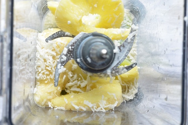 overhead view of sliced kiwi, flaked coconut and pineapple in a blender