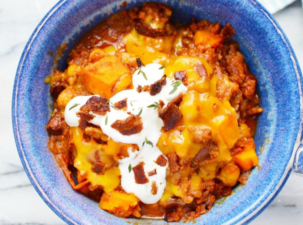sweet potato chili topped with sour cream in a blue bowl on a white counter