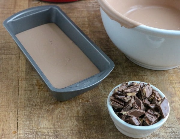 chocolate ice cream mixture in a metal pan and a white bowl next to a white bowl of chocolate pieces on a brown table