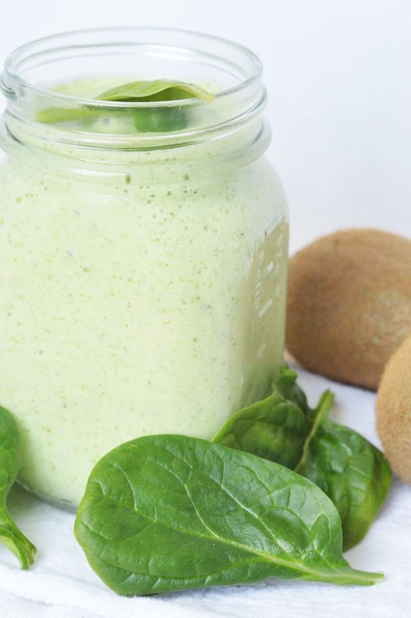 an easy green smoothie in a mason jar next to spinach leaves and kiwis on a white background