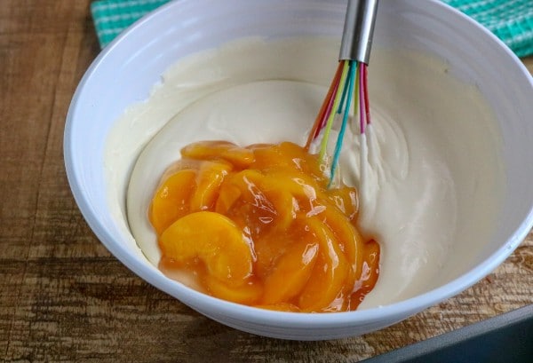 whipped cream and condensed milk and peaches in a white bowl on a green cloth and brown table
