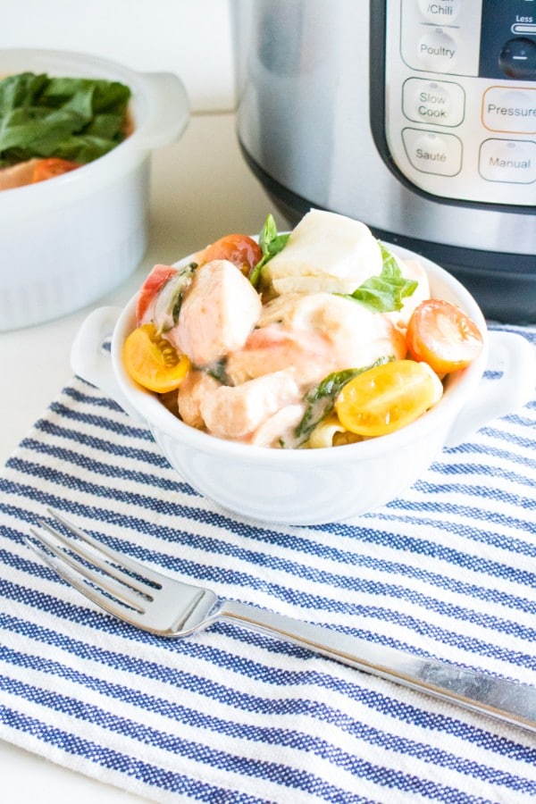 caprese chicken in a white bowl on a blue and white striped linen with an instant pot and another bowl of chicken in the background 