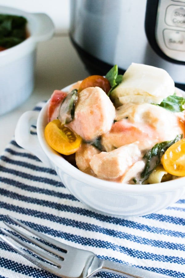 caprese chicken in a white bowl on a blue and white striped linen with an instant pot and another bowl of chicken in the background 
