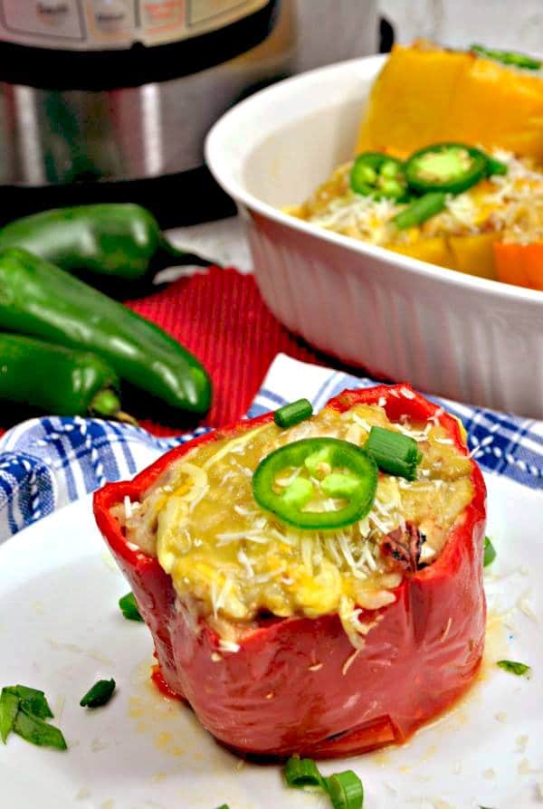 a stuffed pepper topped with cheese, slice of jalapeno and green onions on a white plate on a blue and white linen with a white casserole dish with more peppers, and an instant pot in the background