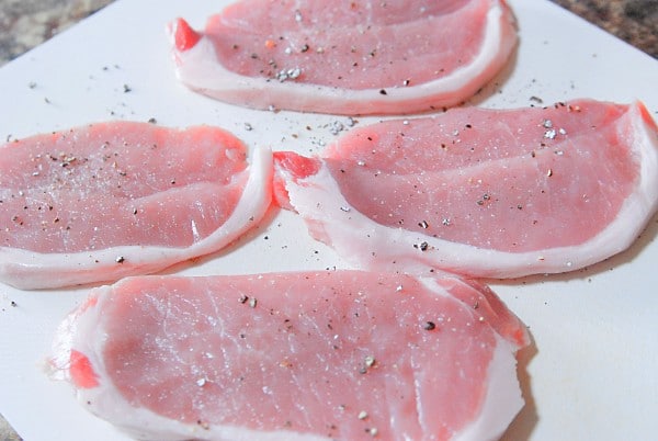 raw pork chops seasoned with salt and pepper on a white cutting board