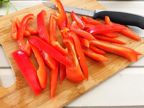 sliced red pepper and a knife on a wood cutting board on a white wood table