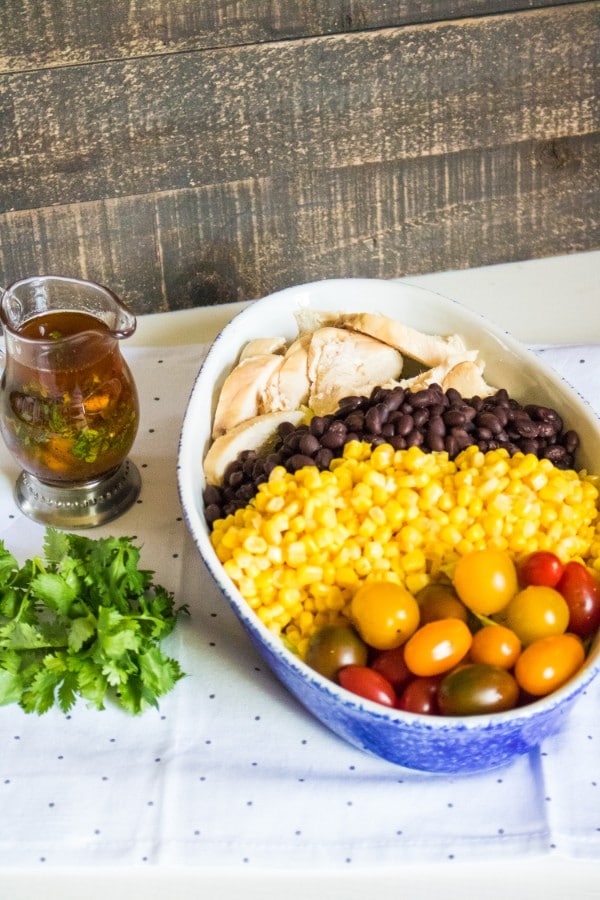 santa fe chicken salad in a large white dish next to a glass of dressing on white and gray polka dotted cloth with a wood wall in the background