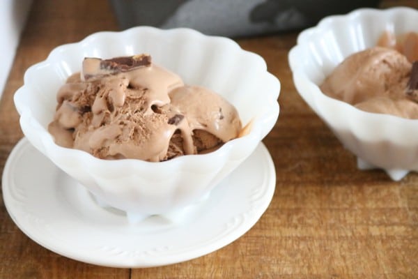 chocolate ice cream in two white bowls, one on a white saucer, on a brown table