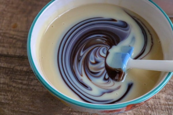 a spatula being used to stir the chocolate syrup into the condensed milk in a bowl on a brown table