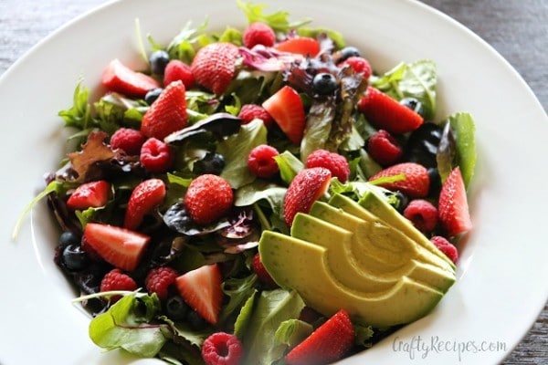 summer berry salad with avocado slices in a white bowl on a wood table
