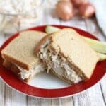 A sandwich made with whole wheat bread filled with Caesar chicken salad, served on a red-rimmed plate with pickle spears in the background.