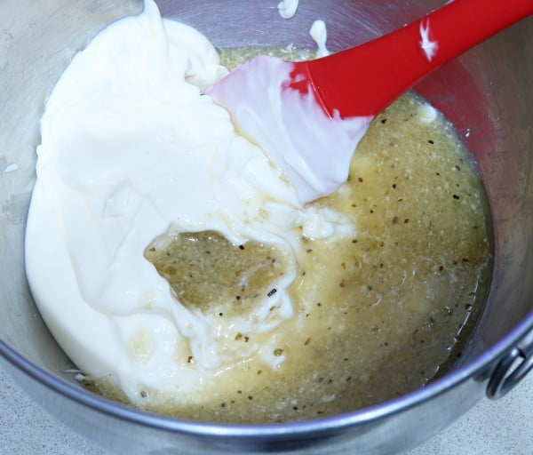 mayonnaise and Caesar dressing being mixedtogether in a large metal bowl with a red spatula