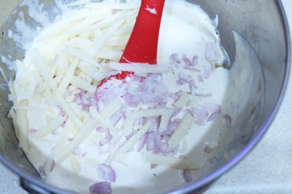 chicken, shallots, and cheese being mixed into the sauce with a red spatula in a metal bowl