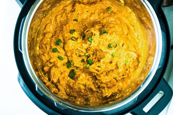 buffalo chicken dip topped with sliced green onions in an instant pot on a white counter