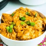 A bowl of creamy buffalo chicken dip garnished with green onions, set on a vibrant patterned tablecloth.