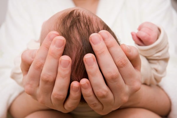 a mother's hands cradling the head of a baby