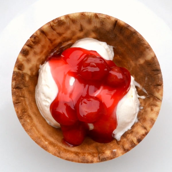 vanilla ice cream topped with cherry pie filling in a waffle cone bowl on a white plate