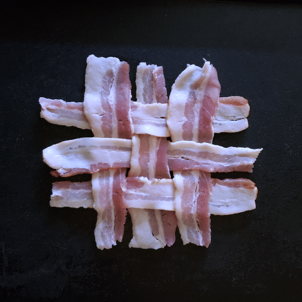 strips of uncooked bacon in a weave pattern on a black background