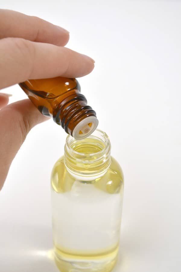 a hand adding essential oil into a spray bottle of poo pourri on a white table.