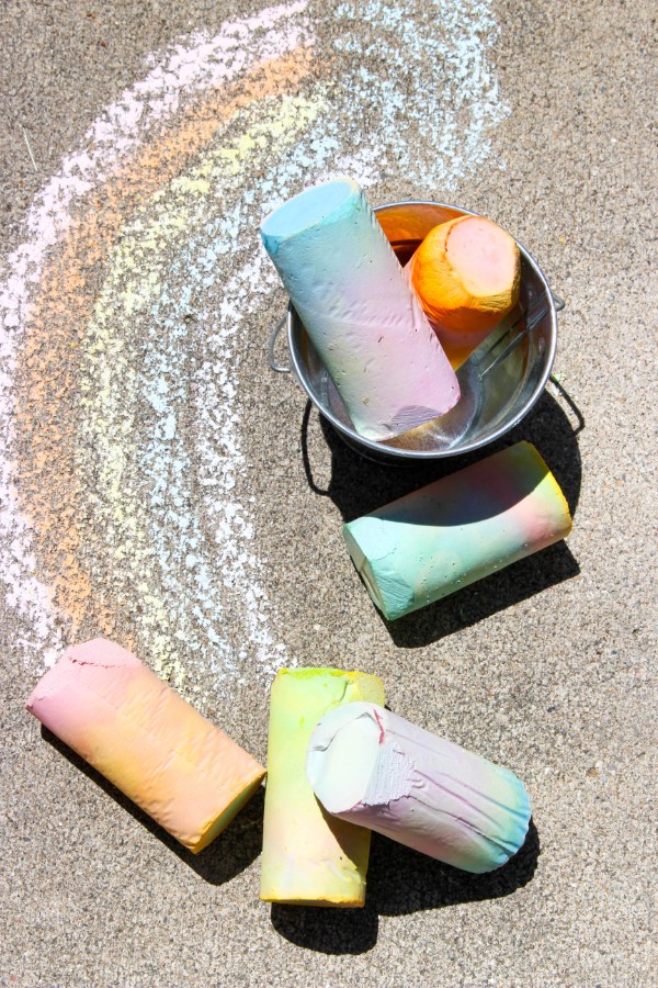 sidewalk chalk on the ground and in a metal can next to a chalk drawing on the ground 