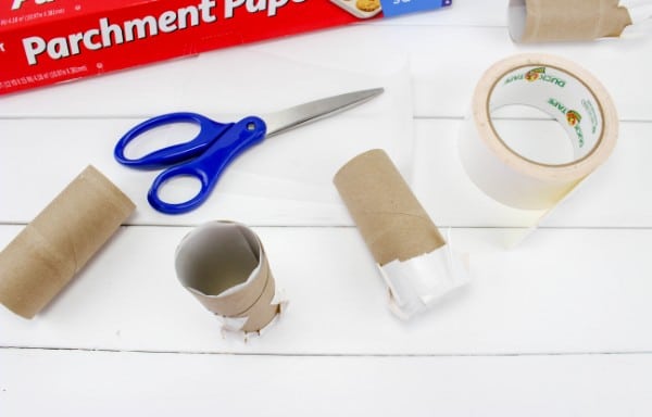 parchment paper, scissors, duct tape, toilet paper rolls on a white wood table