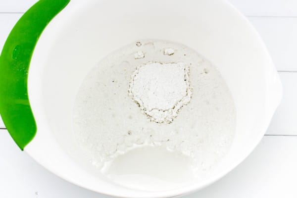 plaster of paris and water in a white and green mixing bowl on a white wood table