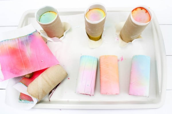 toilet paper rolls full of colored plaster of paris and sidewalk chalk on a white tray on a white wood table